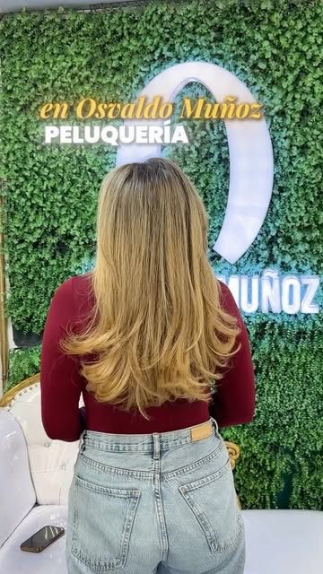 Clienta de espaldas con un rubio largo frente al muro verde con la O iluminada