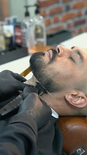 Barbero perfilando la barba de un cliente con máquina
